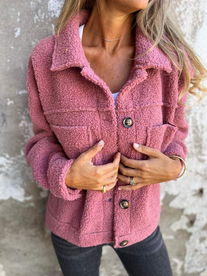 Person wearing a pink sherpa jacket against a textured wall background