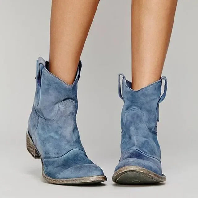 Blue suede cowboy boots worn by a person on a light gray background