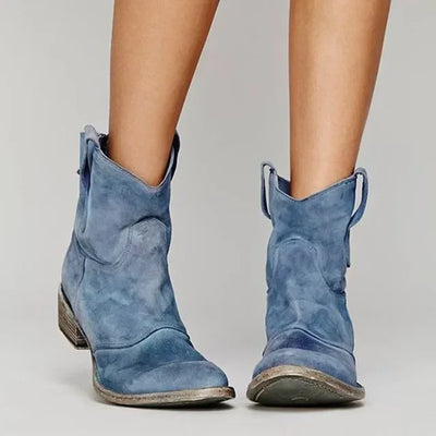 Blue suede cowboy boots worn by a person on a light gray background