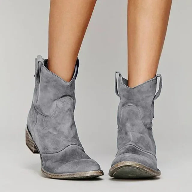 Gray suede ankle boots worn by a person on a plain background