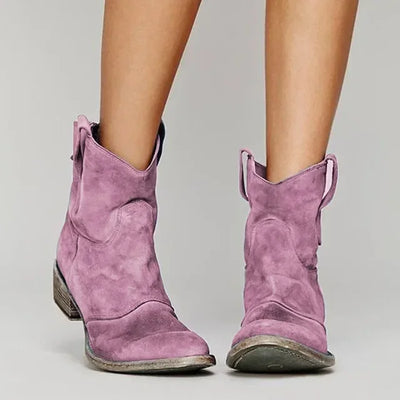 Purple cowboy boots worn by a person on a plain background