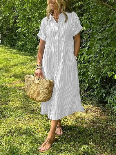 Woman in a white striped dress holding a straw bag outdoors.